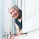 Mujer adulta mayor cuidadora mirando por ventana feliz